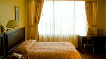 A hotel room with a bed, a desk, a chair, a lamp, and a telephone on the nightstand.