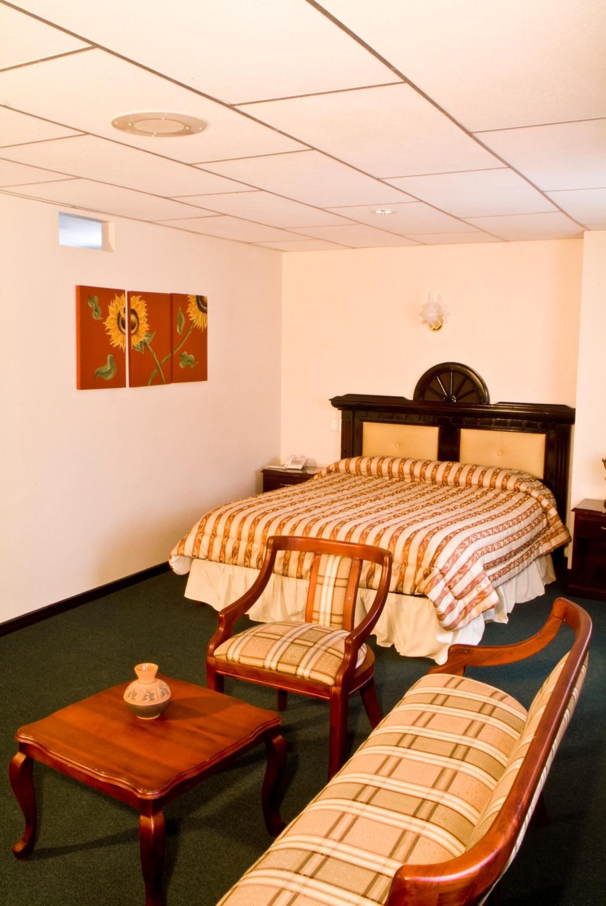 Una habitación de hotel con una cama doble, un banco de madera, una mesita pequeña y un reloj en la pared.