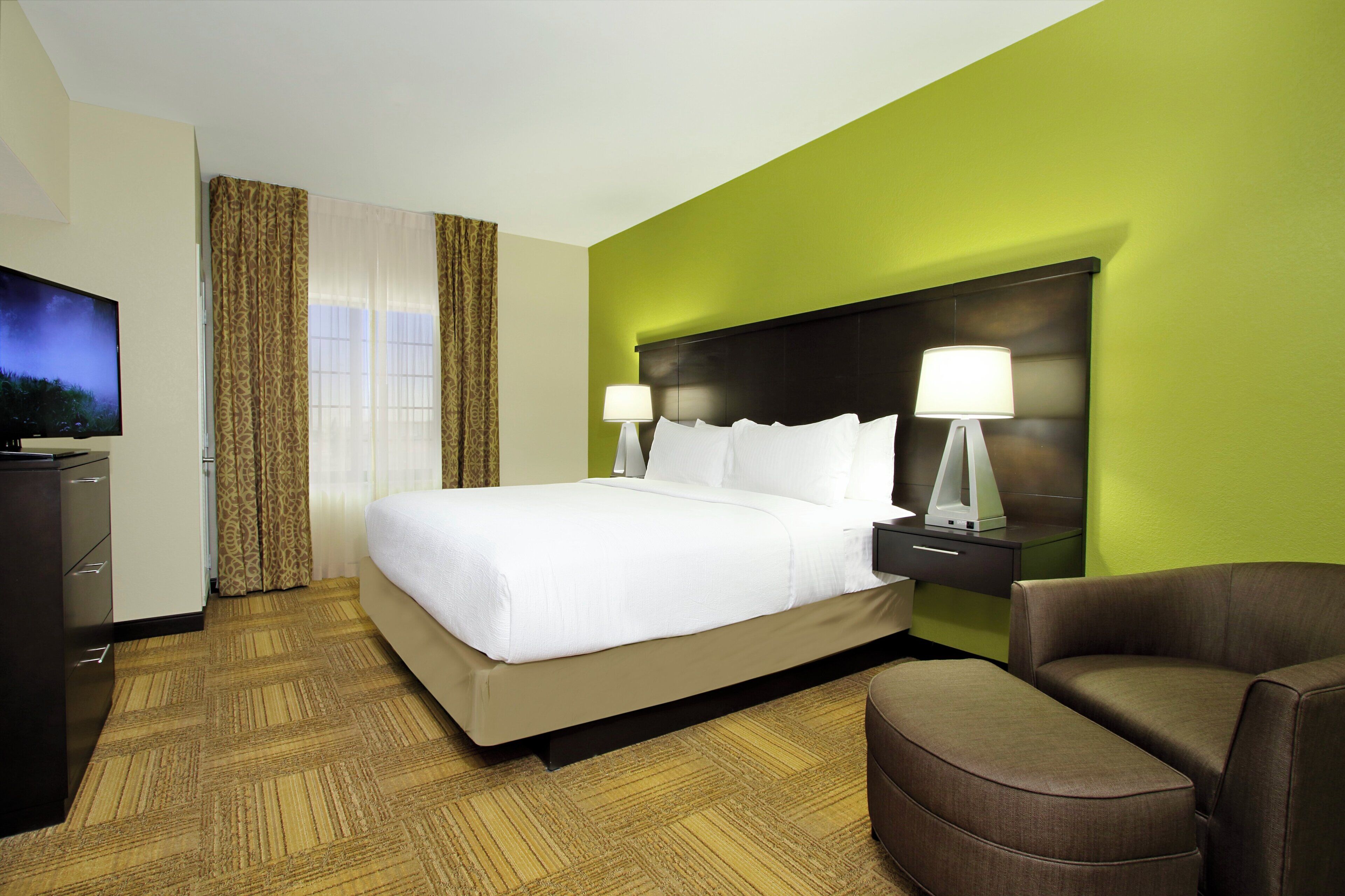 Una habitación de hotel con una cama, televisión, escritorio y una silla.
