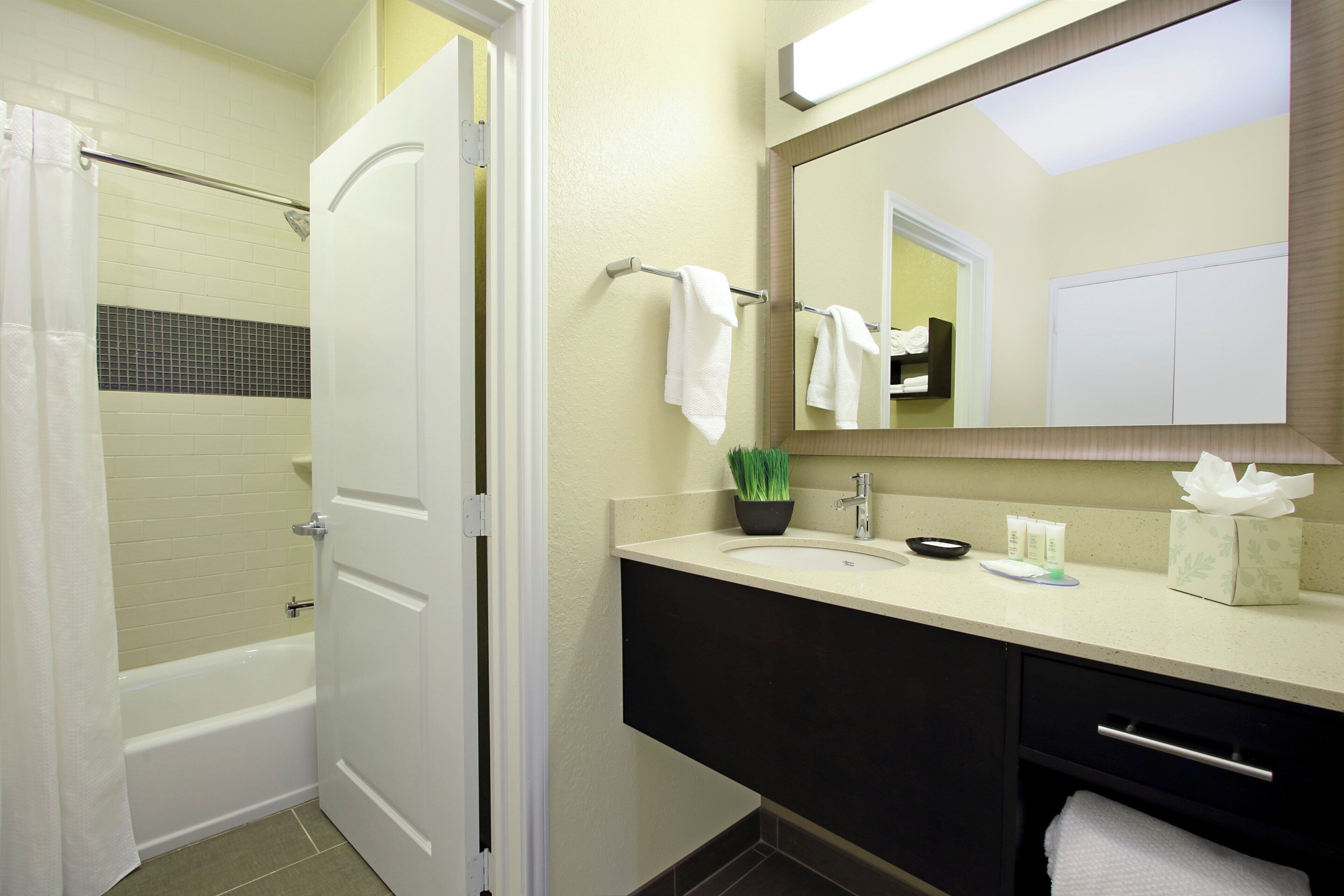 Een badkamer met een bad, een wastafel met toiletartikelen, een spiegel en een handdoekhouder.