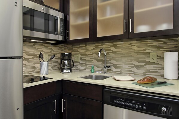 Una cocina moderna con armarios oscuros, un refrigerador de acero inoxidable, un microondas, una cafetera y un lavavajillas.