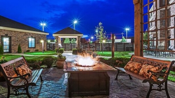 An outdoor patio with stone flooring, two wooden benches, a central fire feature, and a gazebo in the background. - Staybridge Suites Odessa - Interstate HWY 20 by IHG (Odessa)