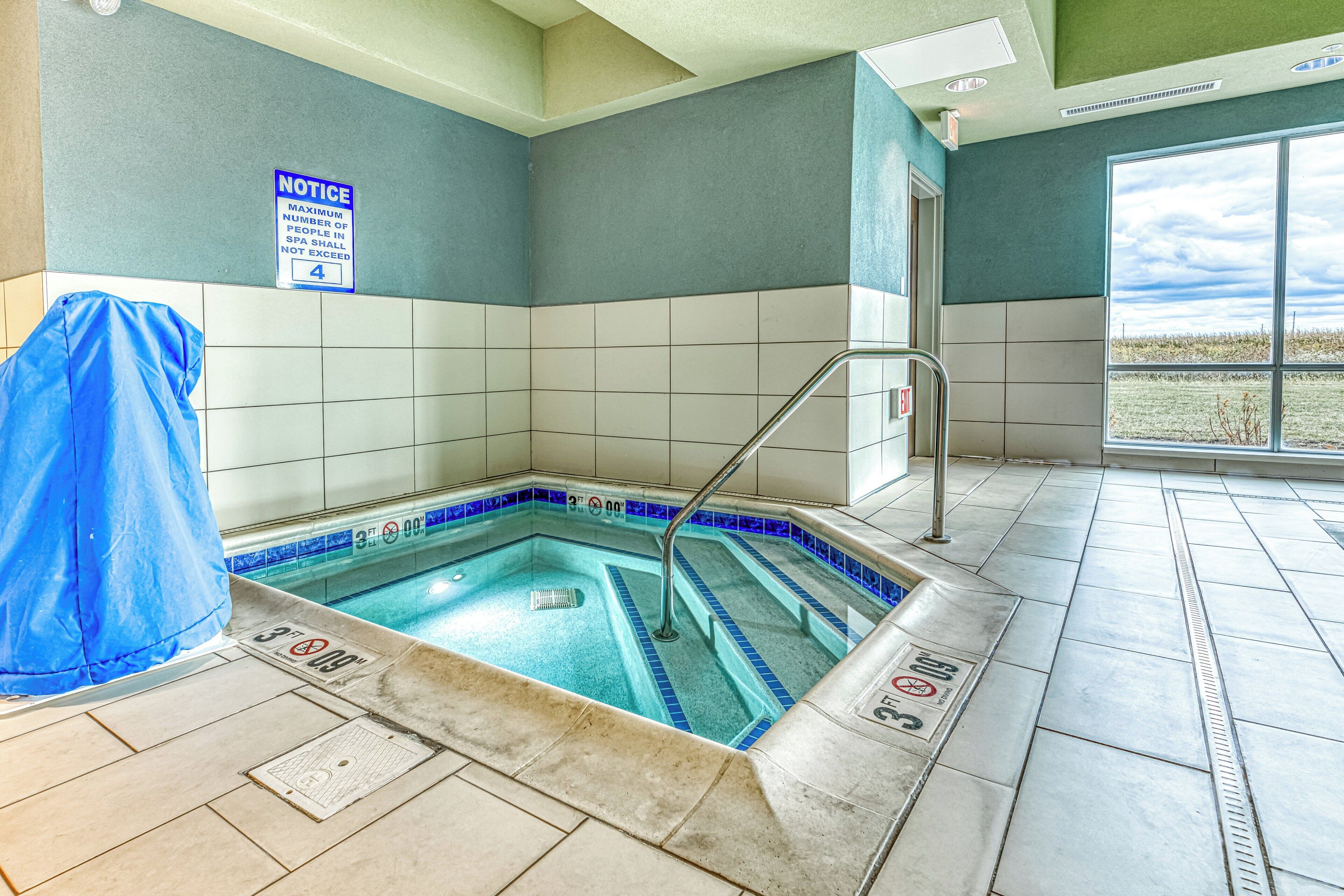 Un espace de détente avec un jacuzzi, des murs carrelés et une bâche bleue recouvrant une piscine.