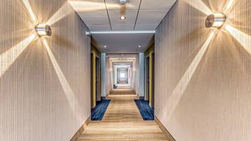 A hotel corridor with a wooden floor, light-colored walls, and a ceiling with recessed lighting.