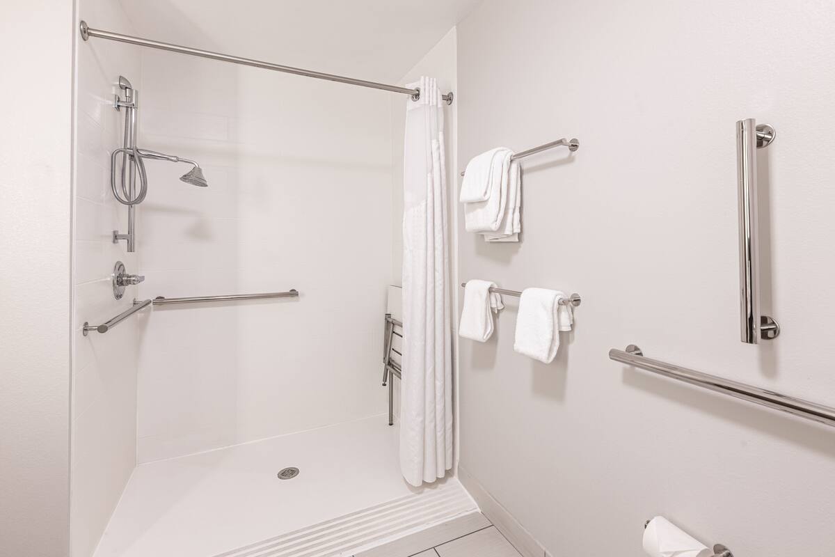 Ein modernes Badezimmer mit begehbarer Dusche, Haltegriffen, einem Handtuchhalter und einem Toilettenpapierhalter.