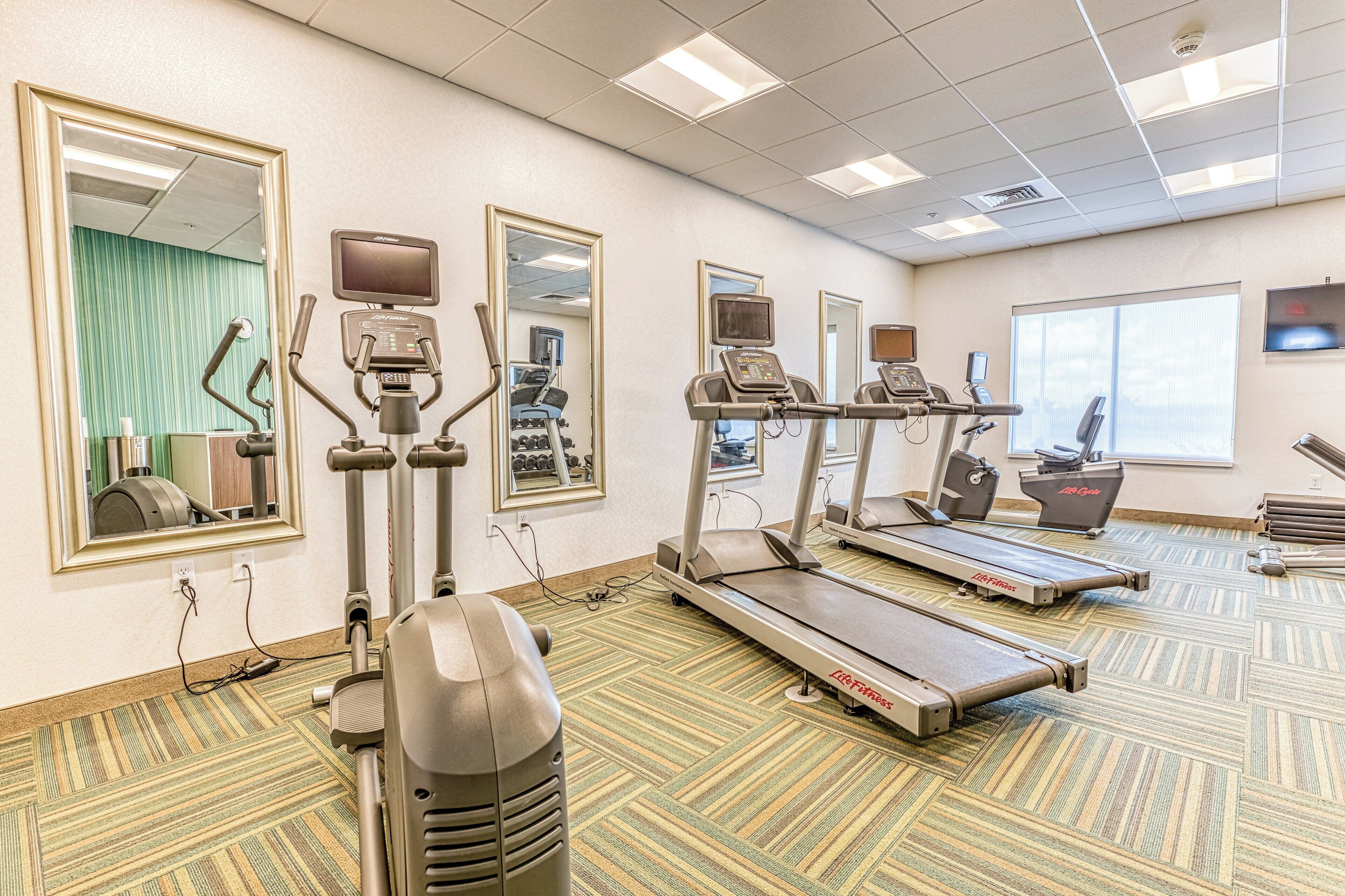 Een fitnessruimte met loopbanden, elliptische trainers en krachttrainingsapparatuur.