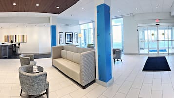 A modern lobby with a reception desk, seating area, and a glass door entrance.