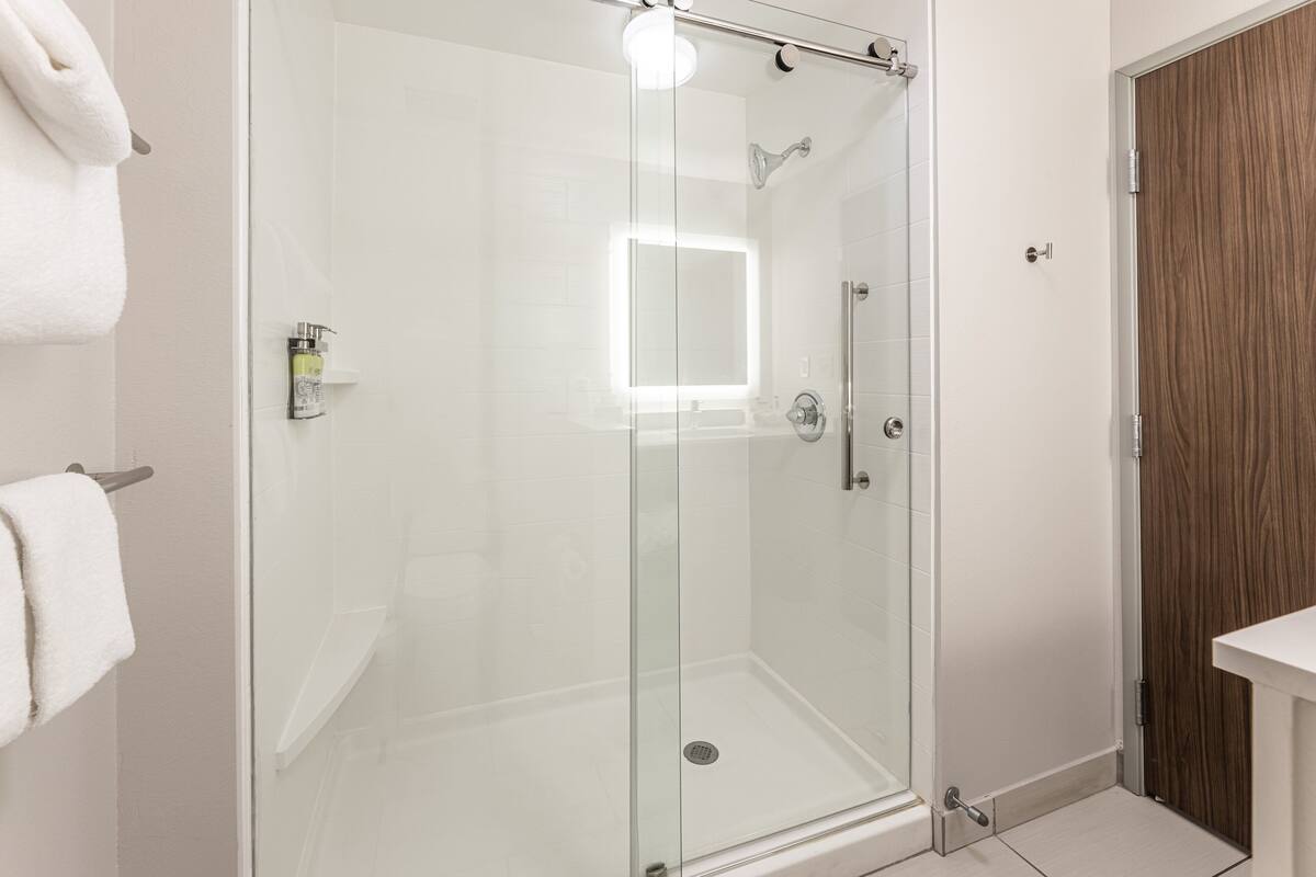 Ein modernes Badezimmer mit einer Glaskabine, einer Holztür und einem weißen Waschbecken.