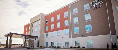 A Holiday Inn Express & Suites hotel with a modern design, featuring a mix of brick and stucco exterior, multiple windows, and a covered parking area.