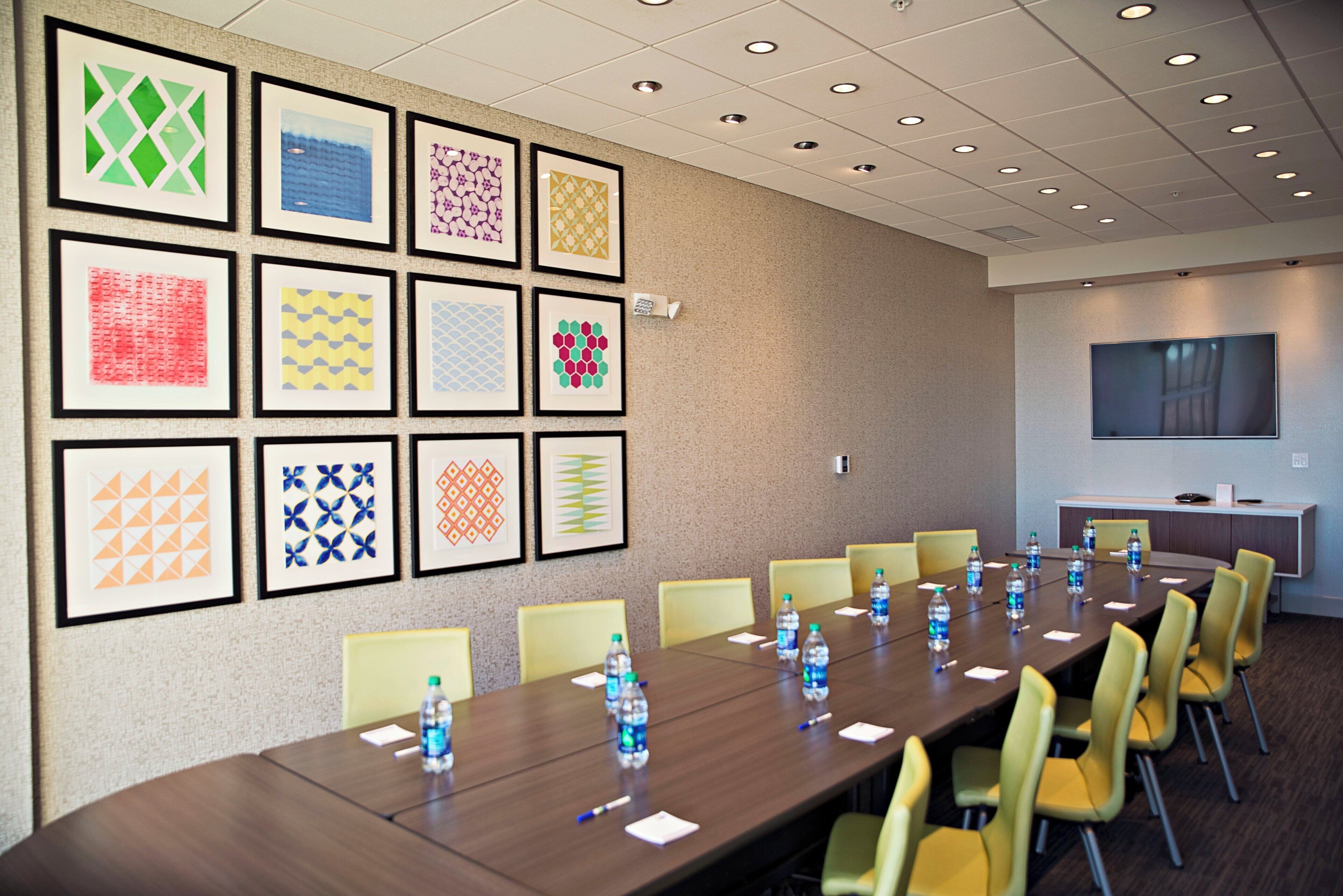 A conference room with a long table, chairs, framed artwork on the wall, and a television on the opposite wall.
