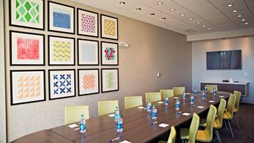 A conference room with a long table, chairs, framed artwork on the wall, and a television on the opposite wall.