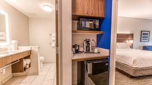 A hotel room with a kitchenette, a bed, a bathroom, and a blue accent wall.