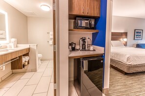 A hotel room with a kitchenette, a bed, a bathroom, and a blue accent wall.