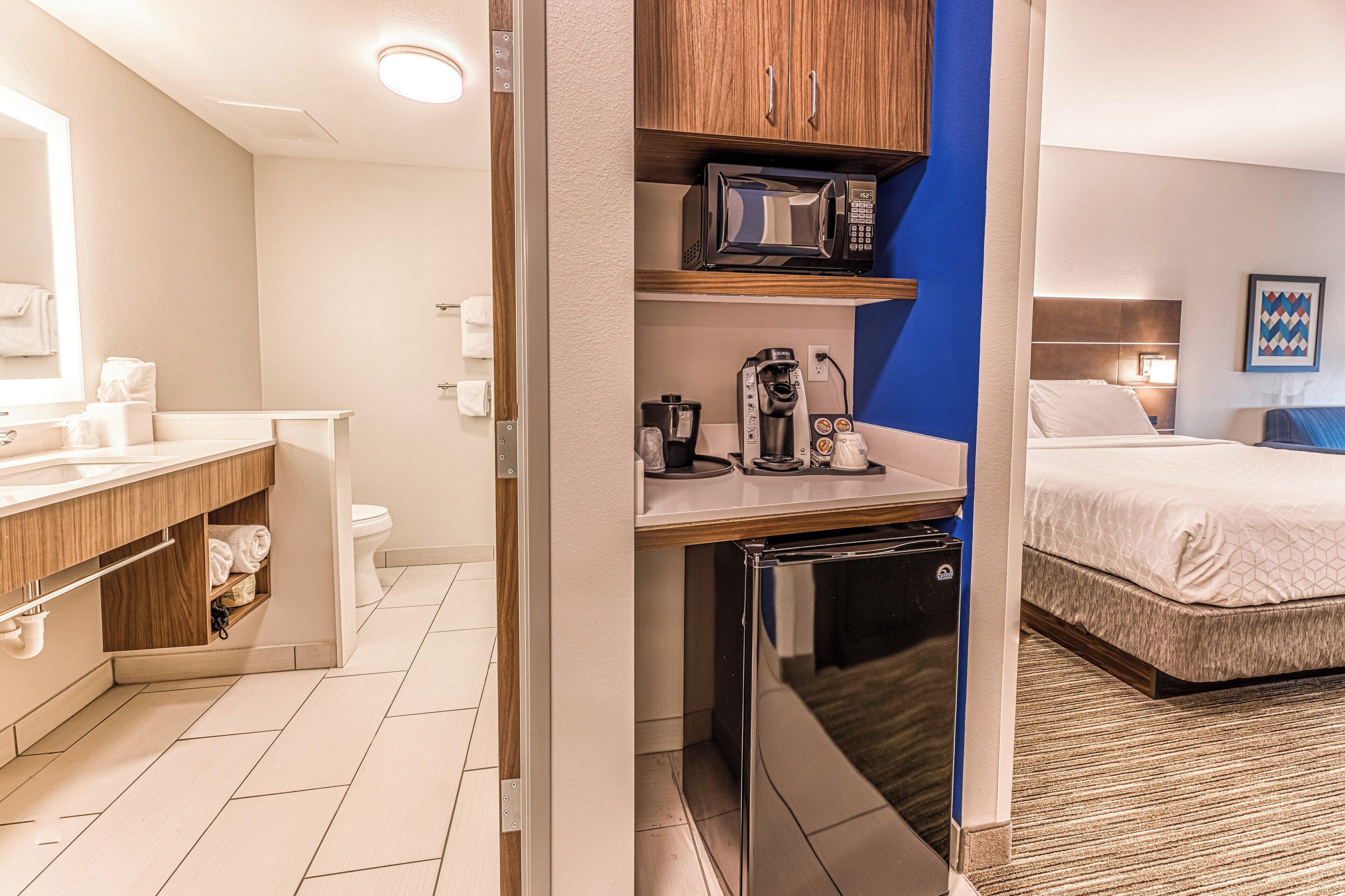 A compact hotel room with a kitchenette, a bed, and a bathroom.