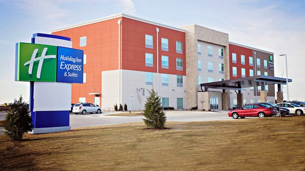 A Holiday Inn Express & Suites hotel with a modern design, featuring a prominent sign, a covered entrance, and a parking lot with several cars.