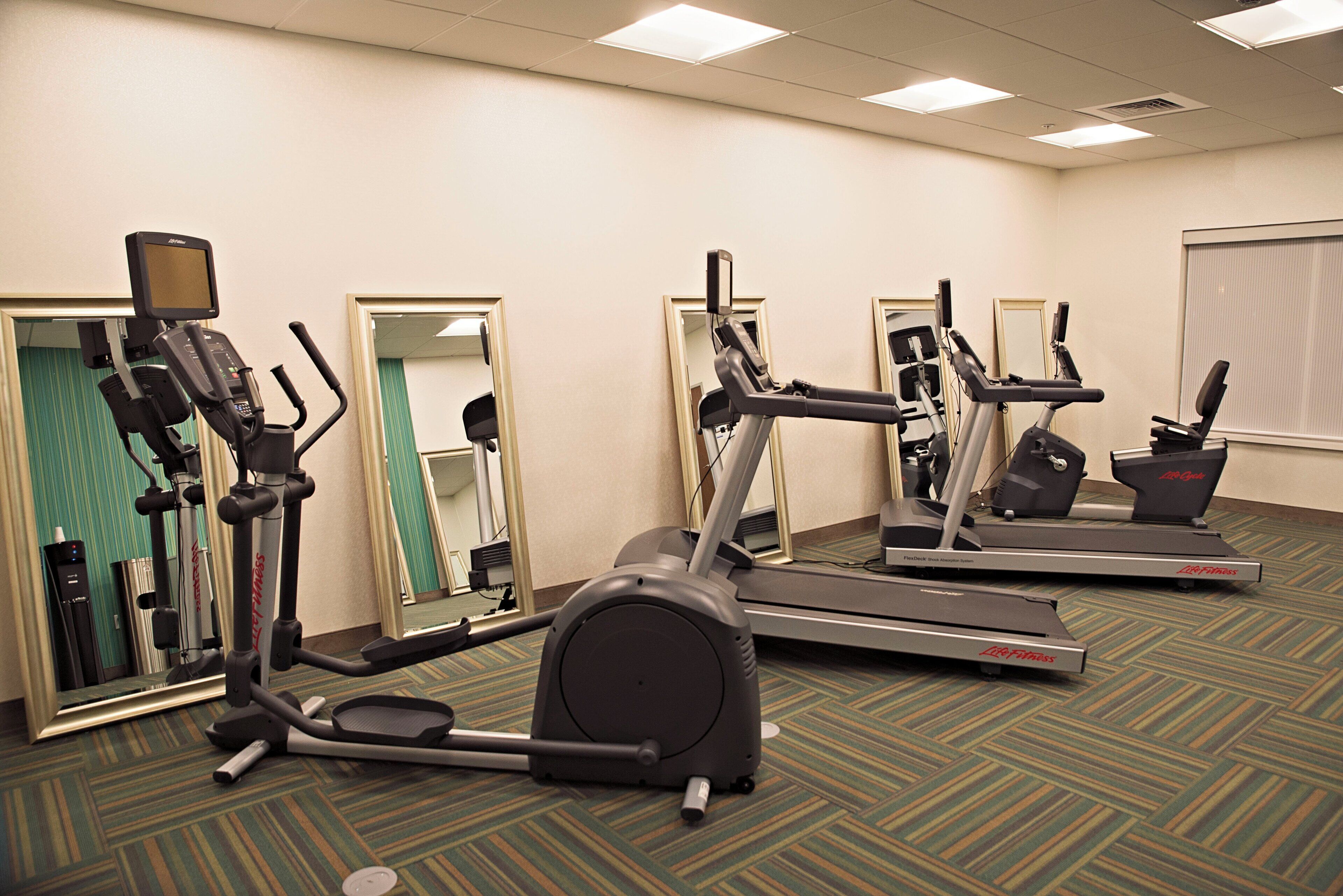 A fitness room with multiple exercise machines, including treadmills and elliptical trainers, and a water dispenser.