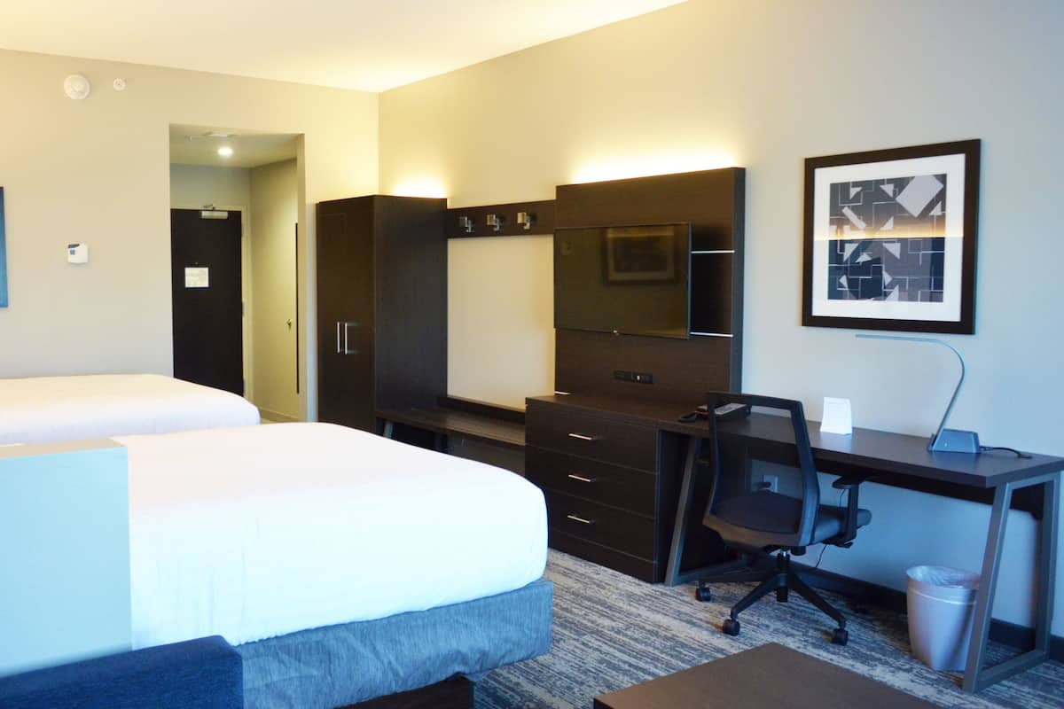 Habitación de hotel con dos camas, un escritorio, una silla, un cesto de basura y un espejo grande.