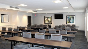 Une salle de conférence équipée de plusieurs tables et chaises, d’un tableau blanc et ornée de deux tableaux.