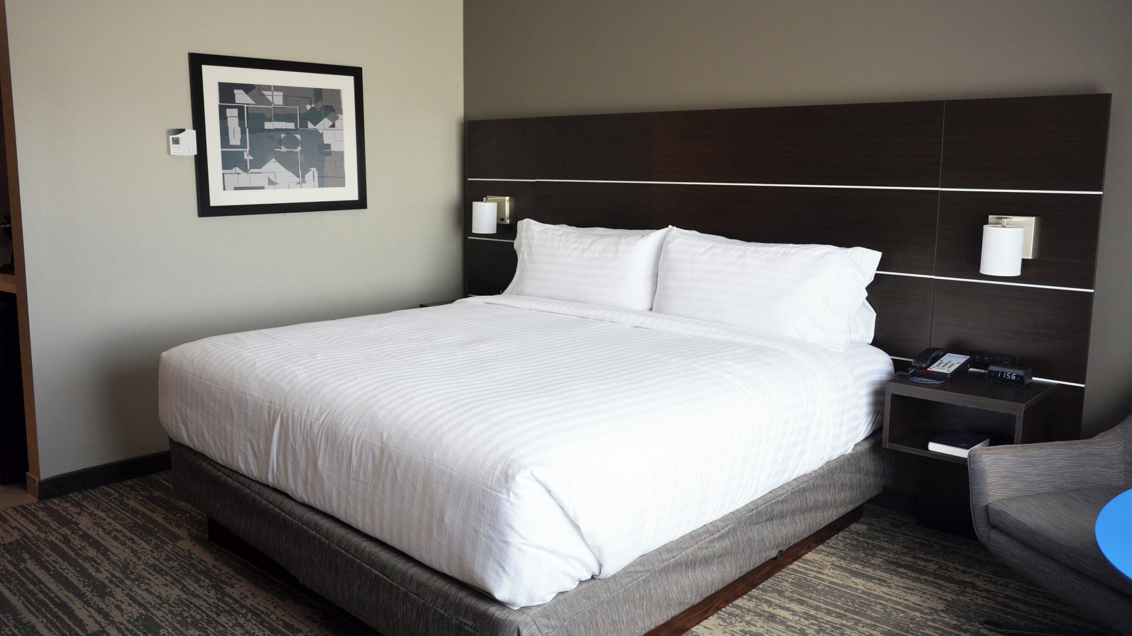 A hotel room with a large bed, a headboard, bedside tables, a chair, and a framed picture on the wall.