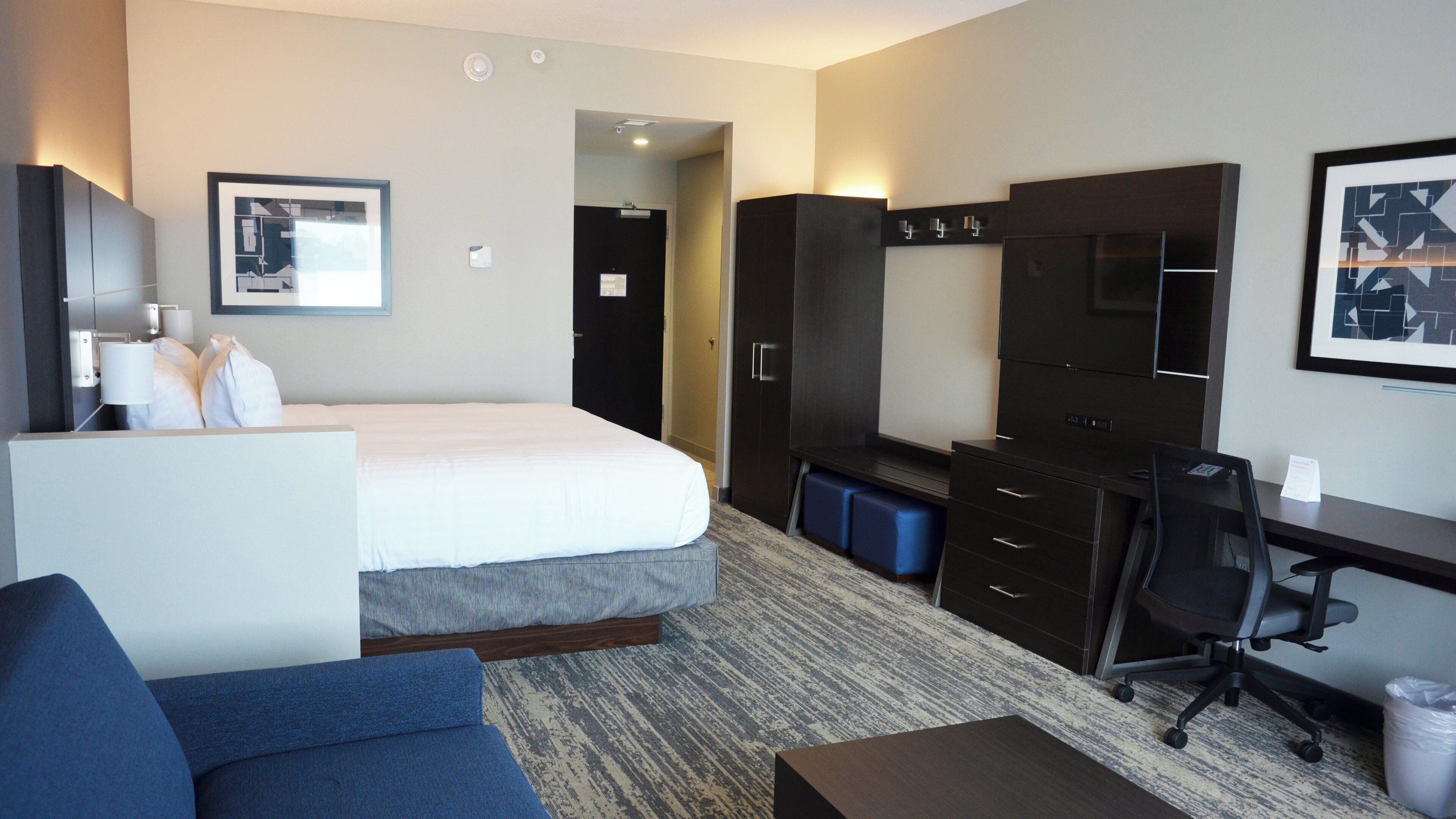 A hotel room with a bed, a desk, a chair, a wardrobe, and a television.