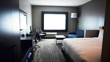 Una habitación de hotel con cama, escritorio, silla, televisor y ventana grande.