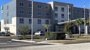 Un hotel de varios pisos con diseño moderno, que presenta una combinación de fachada de piedra y concreto, múltiples ventanas y un estacionamiento con algunos coches.