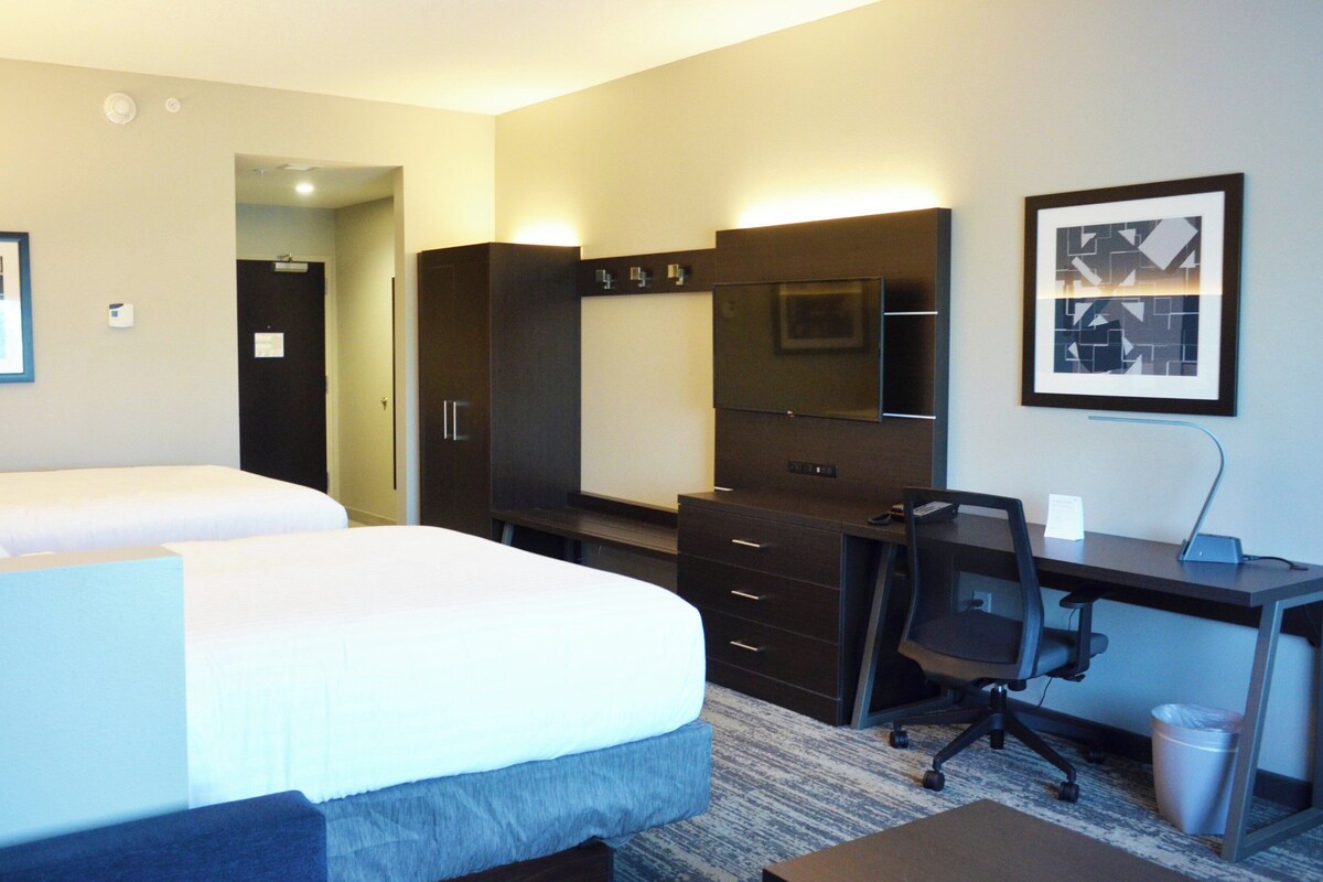 Une chambre d’hôtel avec deux lits, un bureau, une chaise, un miroir et une poubelle.