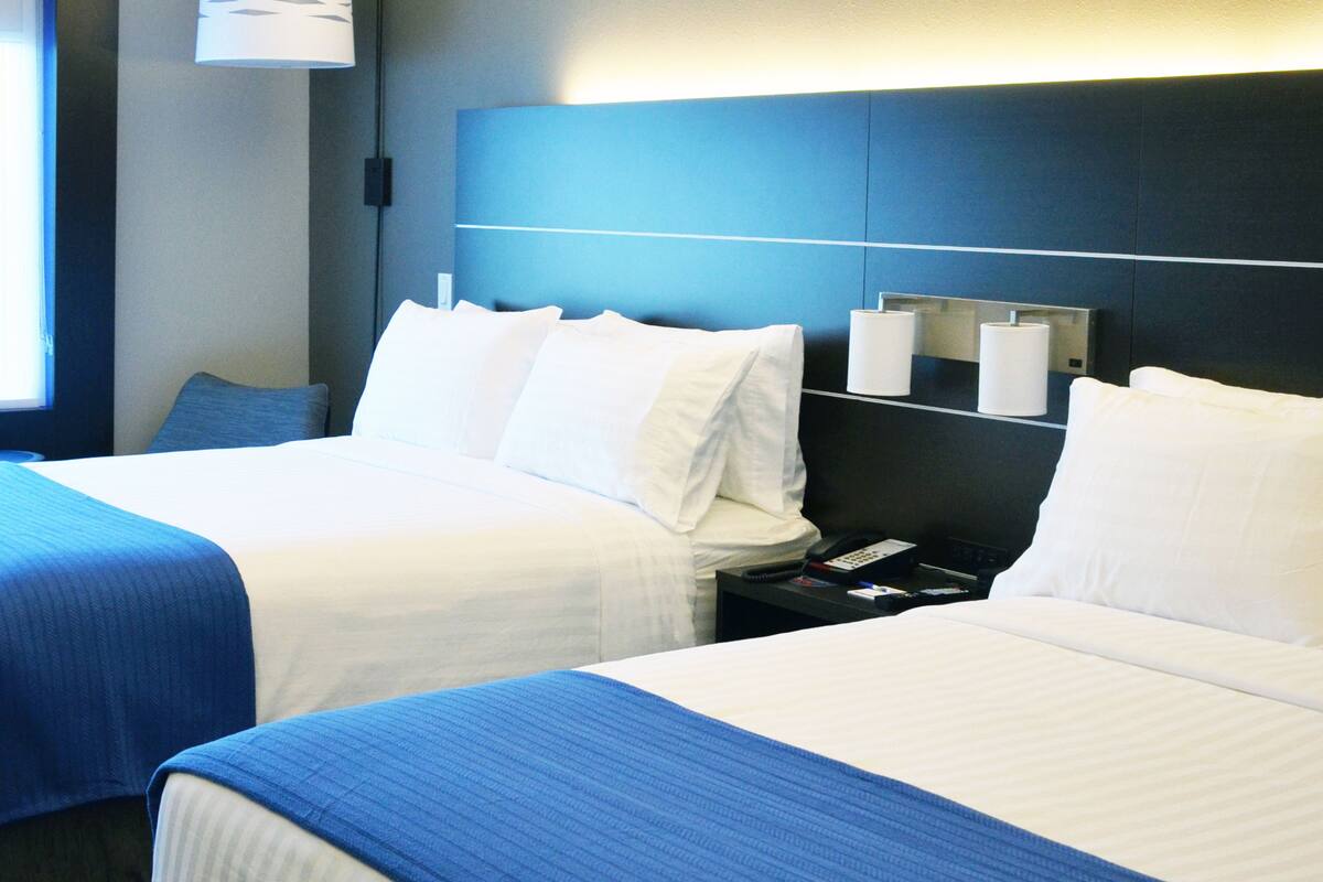 Habitación de hotel con dos camas, una mesita de noche con teléfono y control remoto, y una lámpara fijada a la pared.