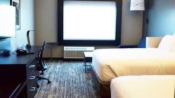 A hotel room with a bed, a desk with a phone and a lamp, a TV, and a window.