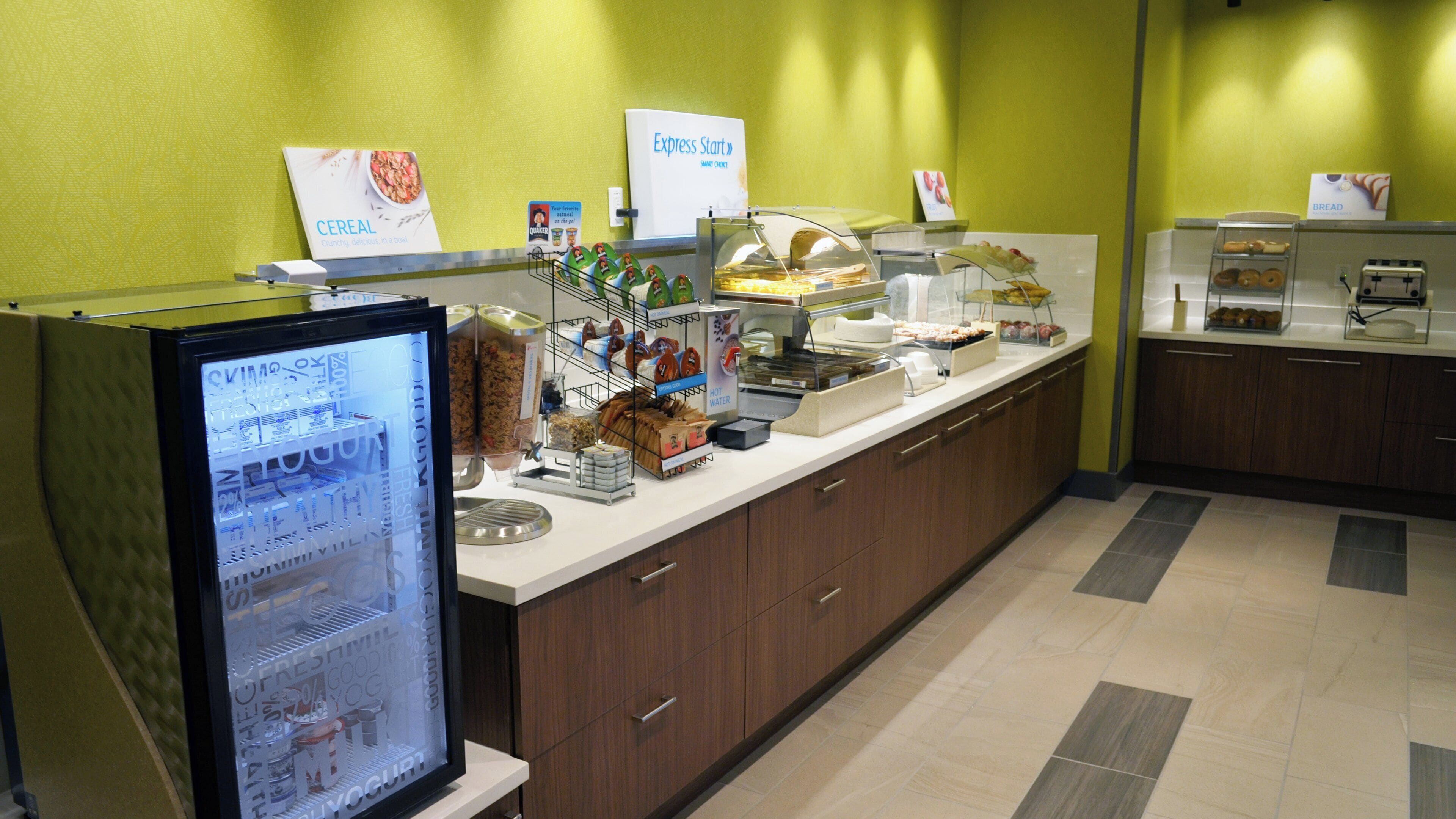 Zona de buffet con diversas opciones de comida, como cereales, yogur y agua caliente.