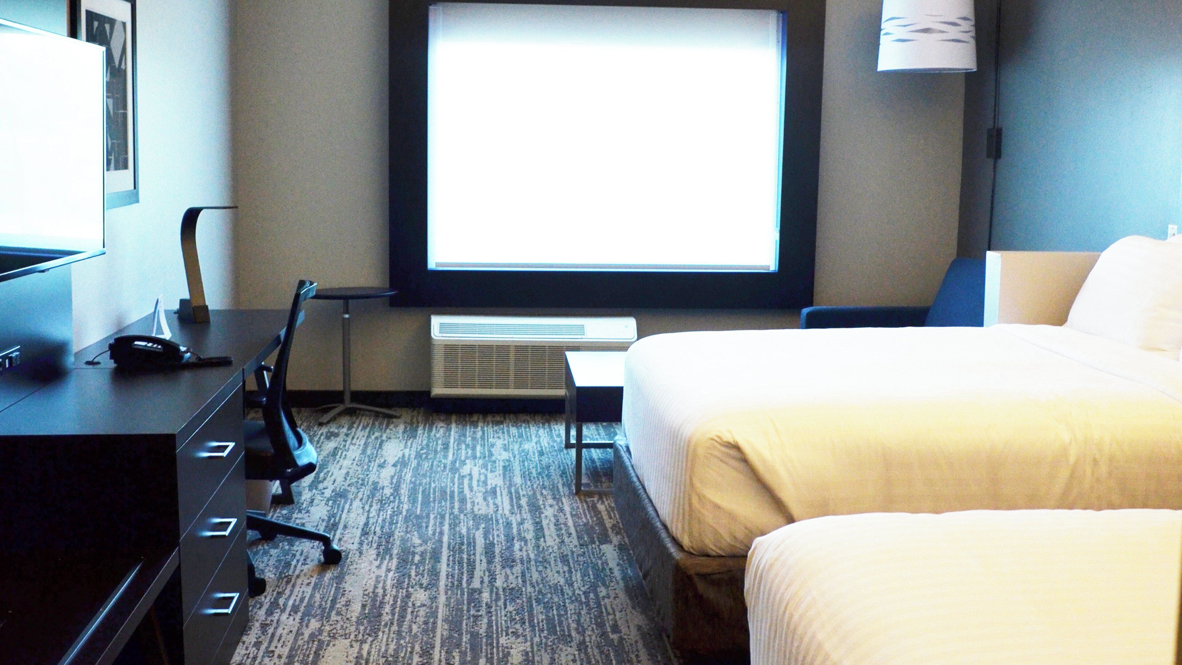 A hotel room with a bed, a desk with a phone, a chair, and a window with a view.