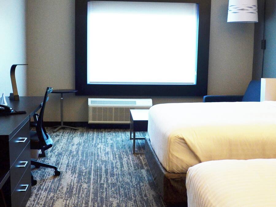 A hotel room with a bed, a desk with a phone, a chair, and a window with a view.
