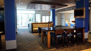 A hotel lobby with a conference table, chairs, a sofa, and a television on the wall. - Holiday Inn Express & Suites Jacksonville W - I295 and I10 by IHG (Jacksonville)