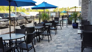Un patio exterior con mesas y sillas, un área de estacionamiento y vistas de la calle.