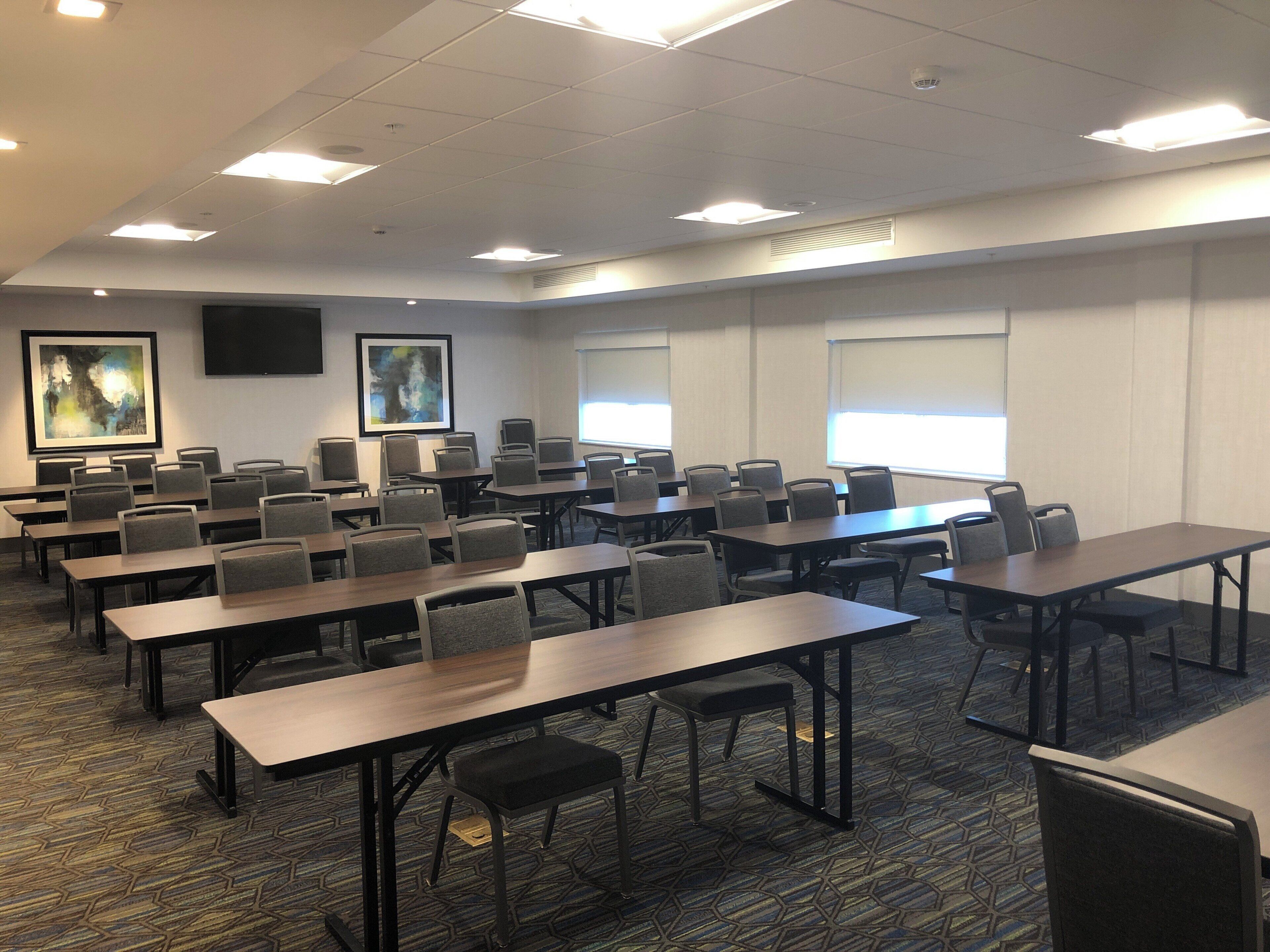 A conference room with multiple tables and chairs, large windows, and artwork on the walls.