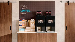 Un espace dédié au café, équipé de deux machines à expresso, d’une cafetière à piston et de différents types de dosettes et de contenants à café.