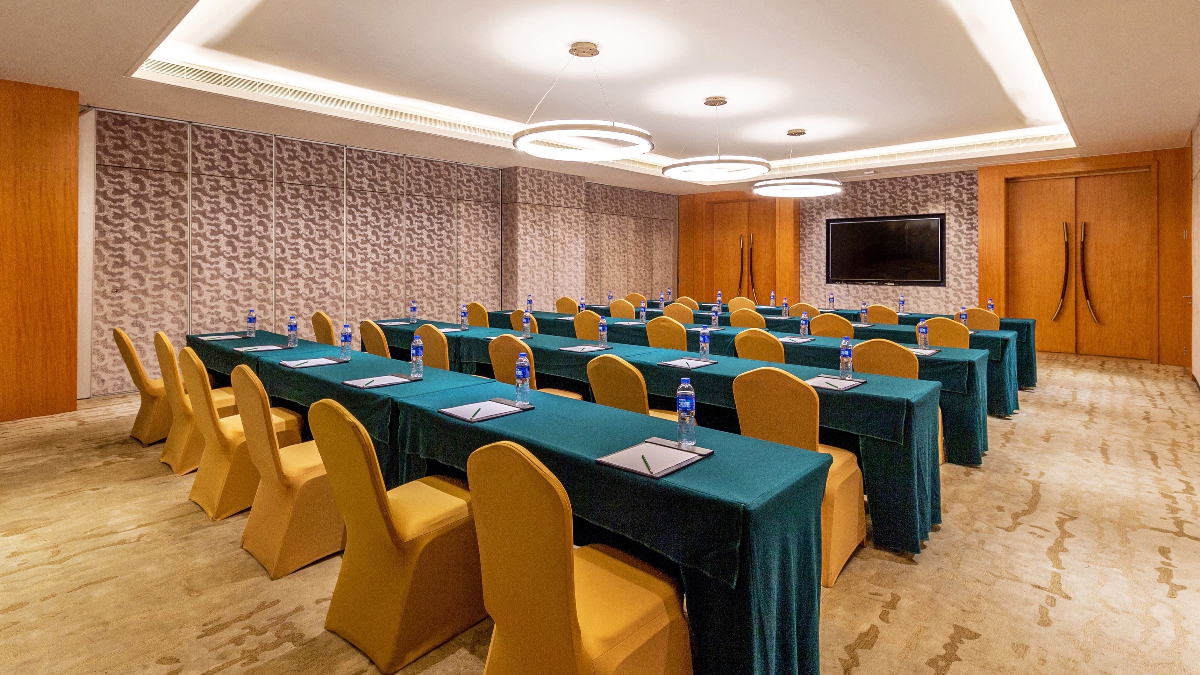 A conference room with multiple tables, chairs, and a large screen.