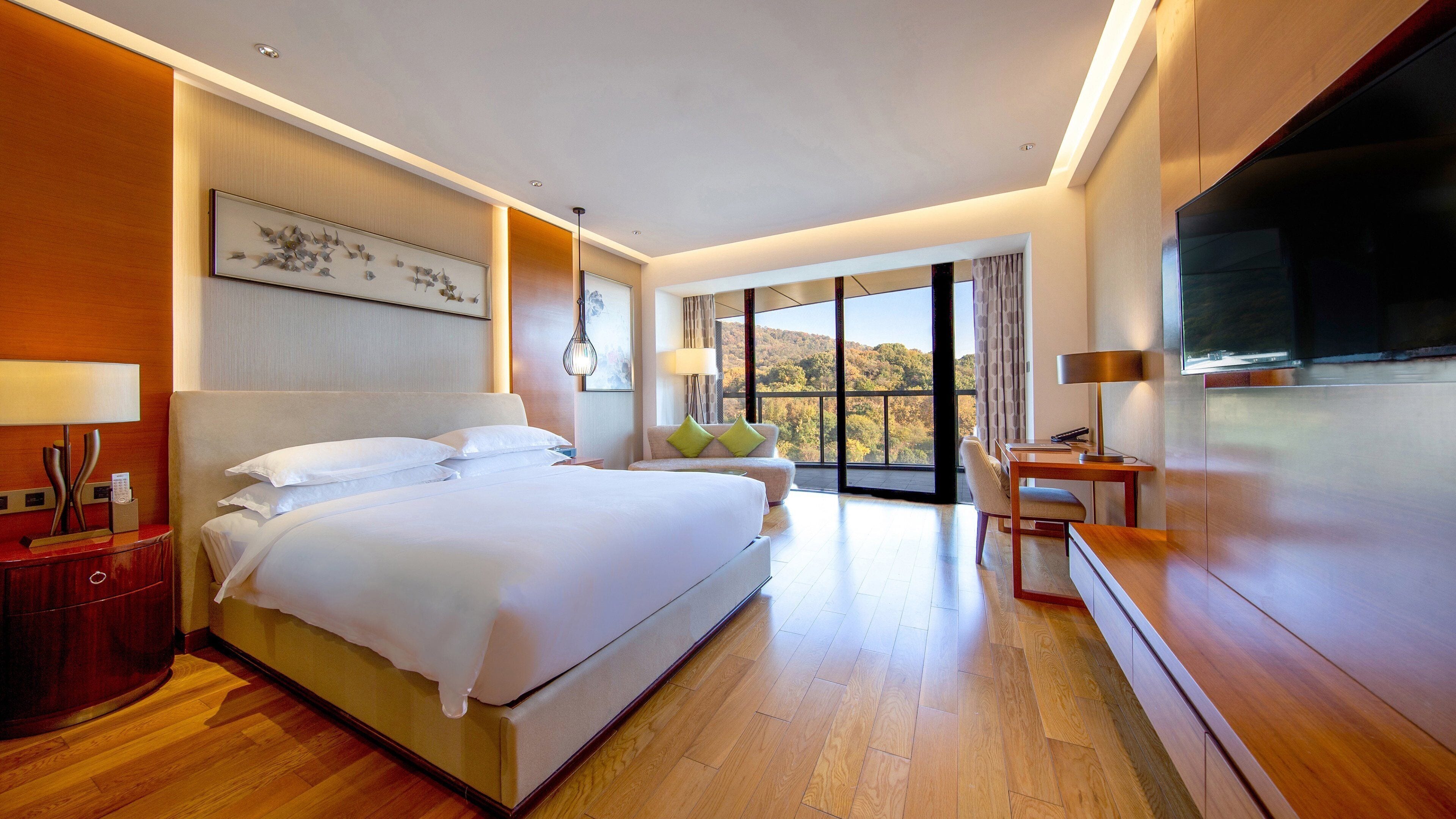 Habitación de hotel con una cama grande, un escritorio con silla, un televisor y un balcón con vistas.