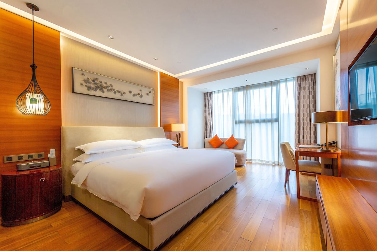 A modern hotel room with a large bed, a desk, a TV, and a window with curtains.