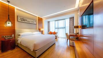 A modern hotel room with a large bed, a desk, a TV, and a window with curtains.