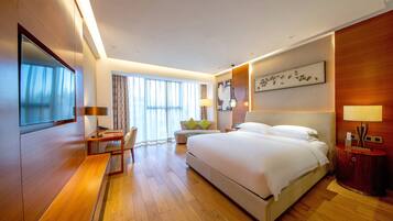 A modern hotel room with a large bed, a desk, a chair, a TV, and a large window with curtains.