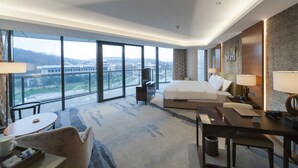 Camera d'albergo con un letto grande, una scrivania, una sedia, una TV e vista sulla città attraverso ampie finestre.