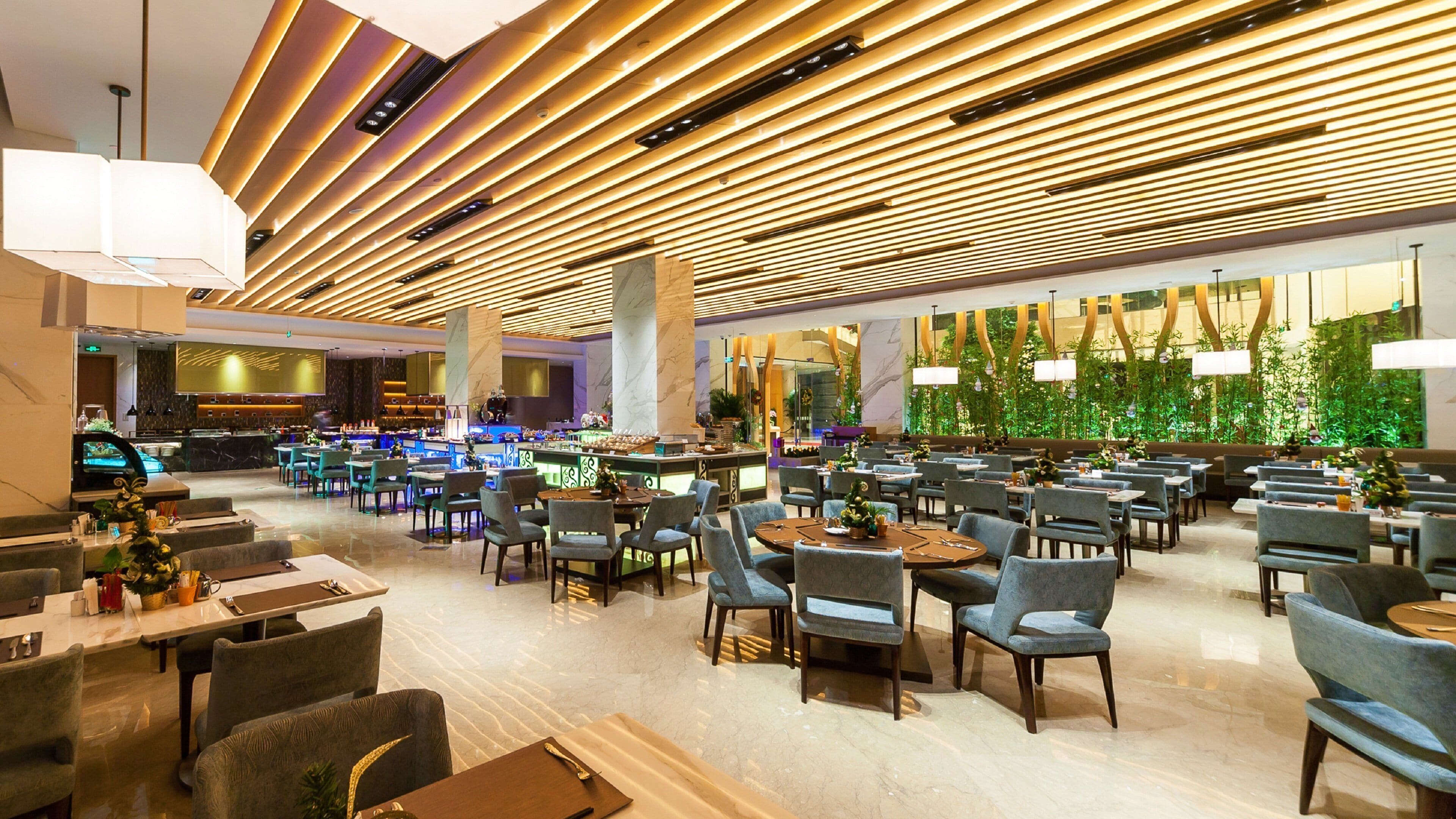 A spacious hotel lobby with multiple seating areas, a bar, and a large green wall with plants.