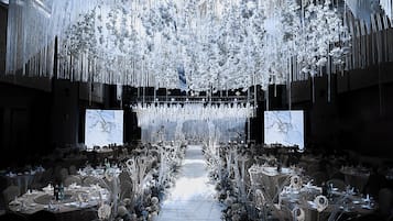 A banquet hall with tables set for a formal event, a central aisle, and hanging floral decorations.