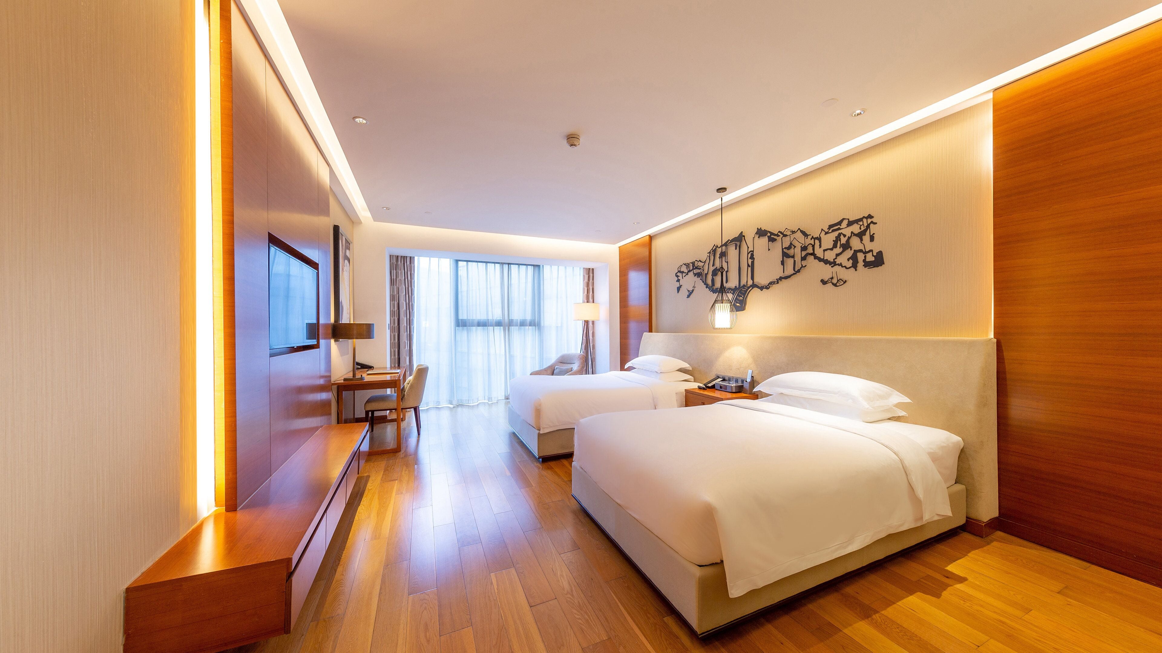 A hotel room with two beds, a desk, a chair, and a large window.