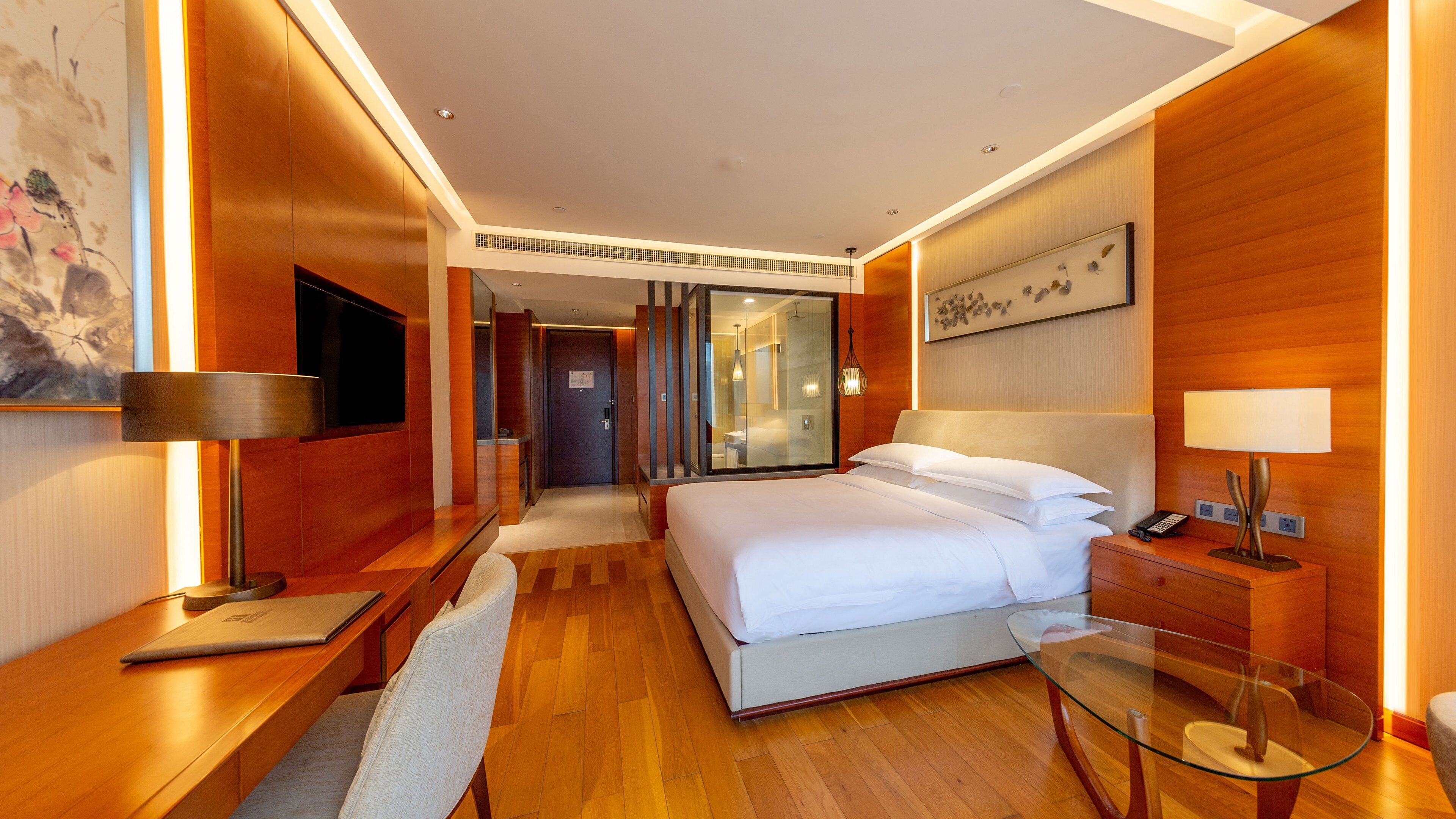 A modern hotel room with a large bed, a desk, a glass table, and a TV.