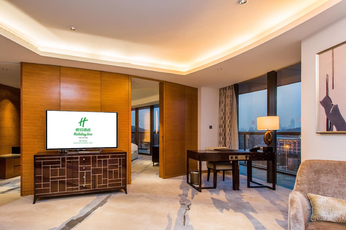 A hotel room with a large TV on a wooden cabinet, a desk with a chair, and a sofa.