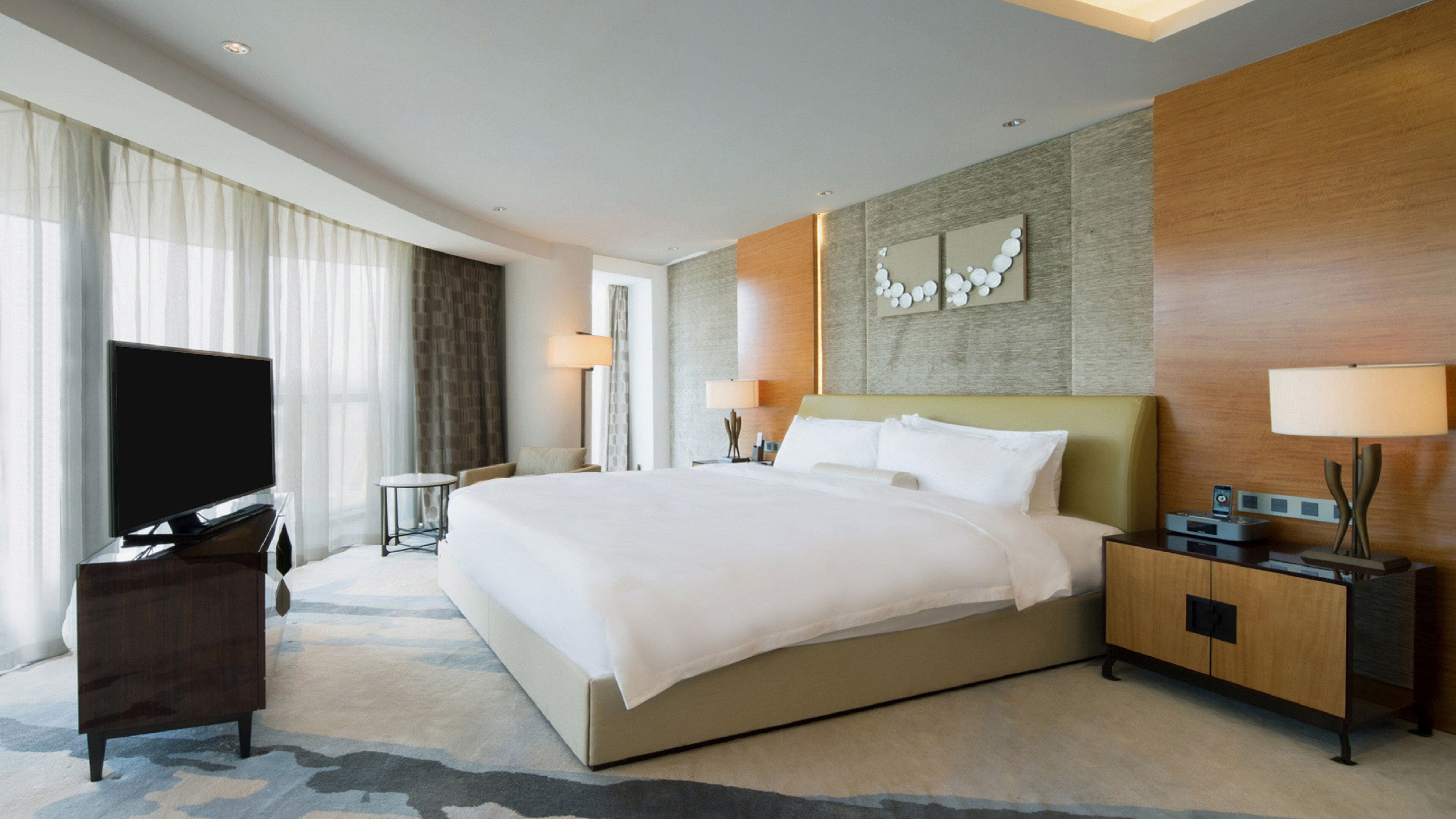 A hotel room with a large bed, a TV, a desk, and a lamp.