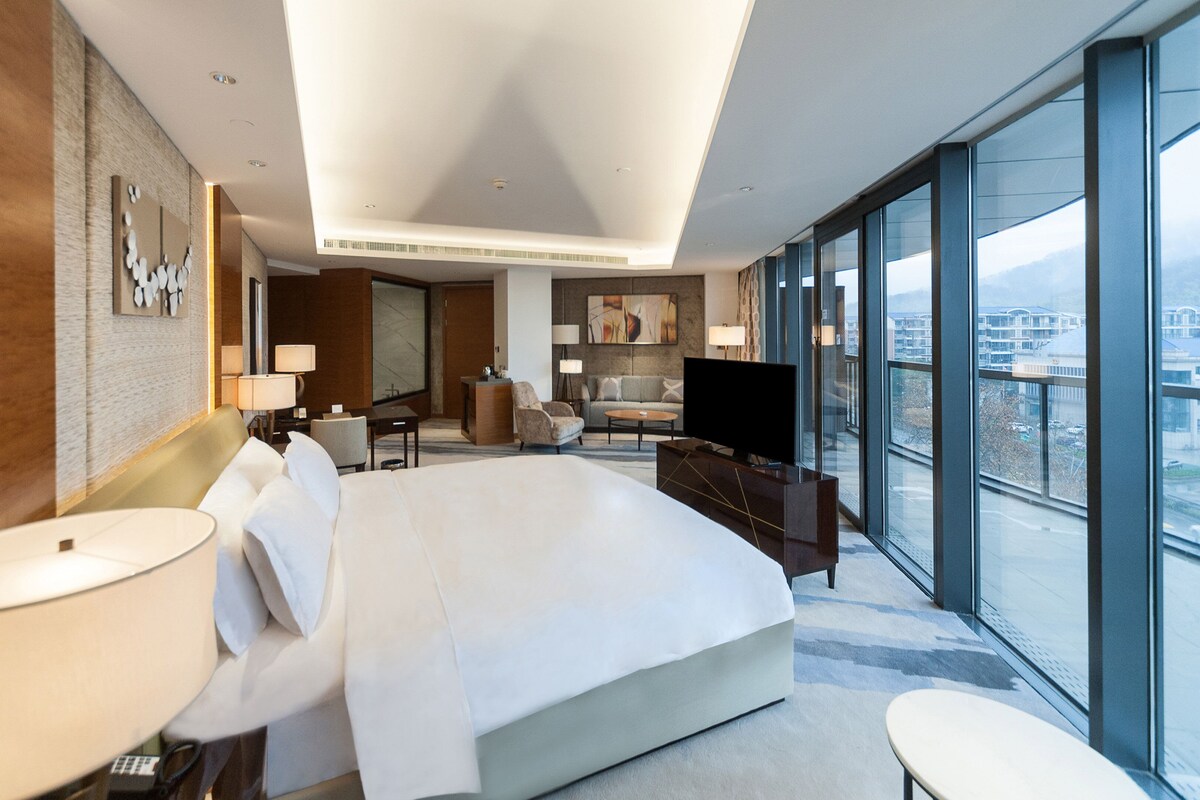 Una habitación de hotel moderna con una cama grande, televisión, escritorio y vistas a la ciudad.