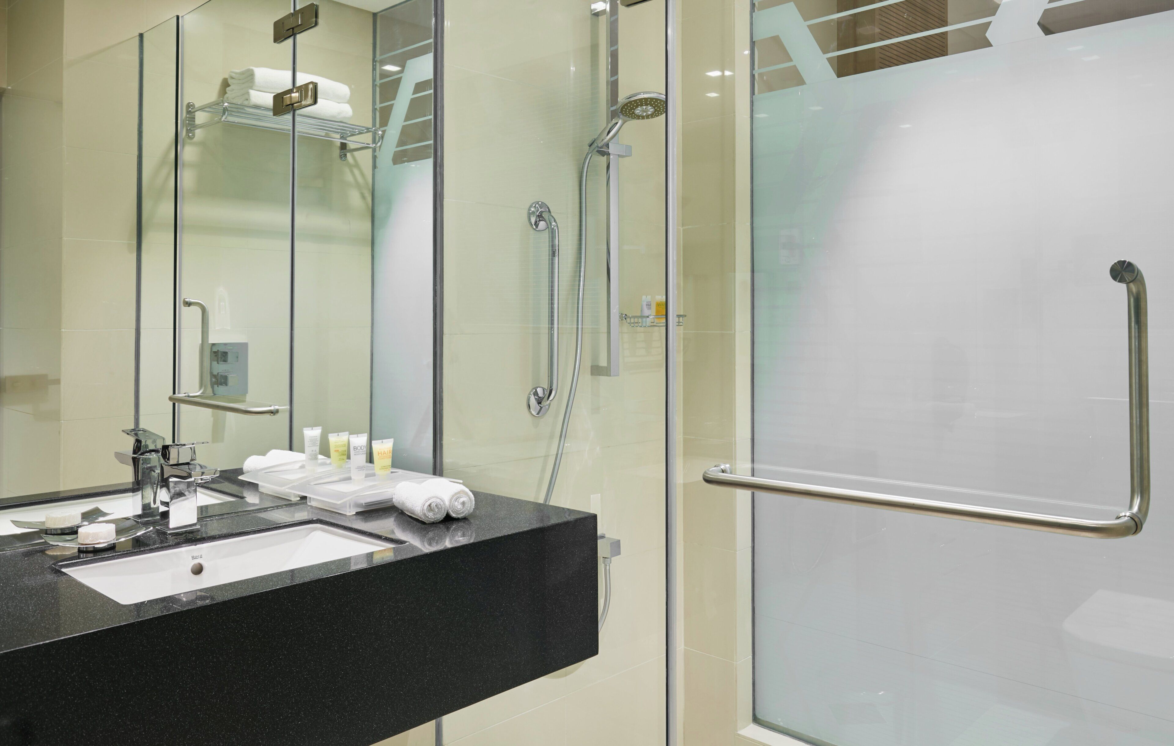 A modern bathroom with a glass shower enclosure, a black countertop, and a glass door with a towel rack.